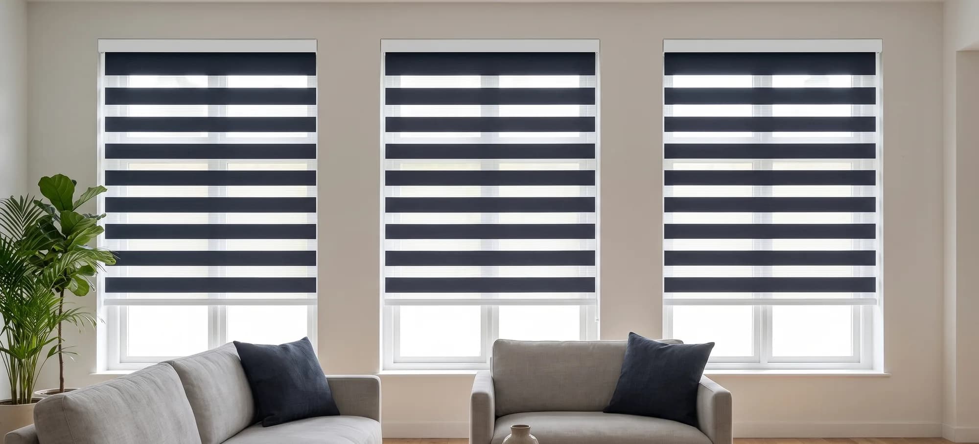 Navy and white zebra shades on three tall windows behind a grey sofa in a bright living room.
